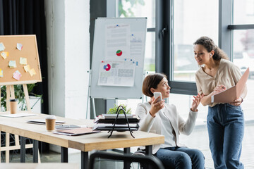 Obraz premium african american businesswoman and her colleague in wheelchair working near blurred flip chart with analytics