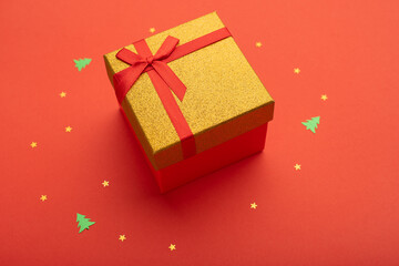 Red and gold gift box on a bright red background with golden stars and little Christmas trees.