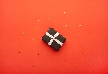 Little gift box with a ribbon on bright red background with stars. Top view, flat lay. 