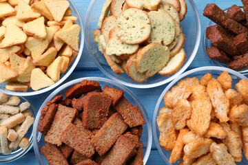 Different crispy rusks in bowls on light blue wooden table, flat lay