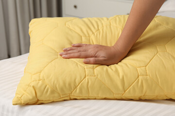 Woman touching soft pillow in bedroom, closeup