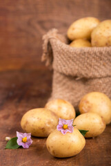 Raw potatoes with flowers in the bag on the wooden background