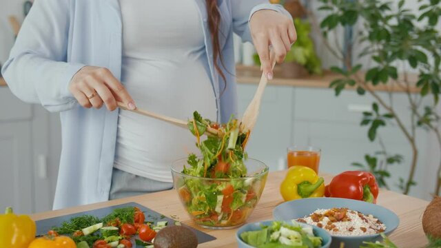 Pregnant Woman Preparing Organic Healthy Food. The Woman Mixes Vegetable Salad in a Bowl in the Kitchen. Healthy Vegetarian and Vegan Diet Concept.