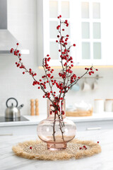 Hawthorn branches with red berries on table in kitchen