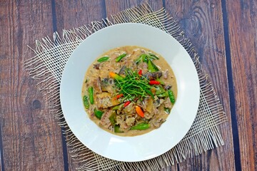 Stir fried mackerel with coconut milk in white plate on wooden table. Authentic Thai food.