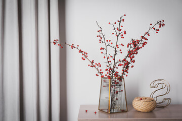 Hawthorn branches with red berries in vase, decorative letter and wicker box on wooden table indoors, space for text