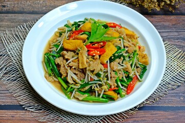 Stir fried tofu with bean sprouts, green chives and minced pork in white plate on wooden table.