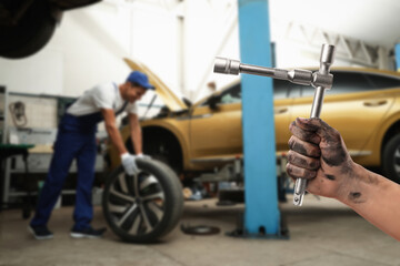 Fototapeta na wymiar Auto mechanic with instrument near broken down car in repair shop, closeup