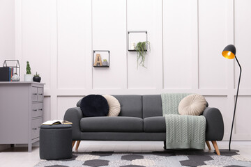Stylish living room interior with comfortable grey sofa and lamp