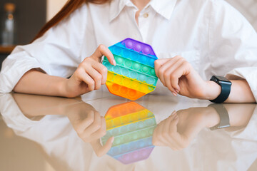 Close-up cropped shot of unrecognizable young woman playing with rainbow pop-it fidget toy sitting...