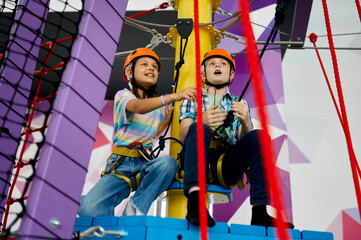 Two children in helmets climb on tightropes