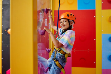 Little girl in helmet poses on climbing wall