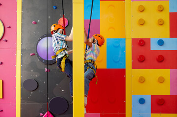 Two children in helmets climb on climbing wall