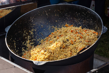Hot pilaf in large cauldron outdoors. Traditional oriental food. Street food concept.