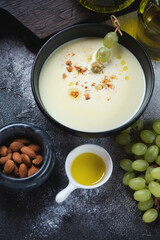 Bowl of ajo blanco or spanish white gazpacho served with grapes, vertical shot on a dark-grey stone background
