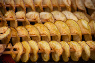 Spiral potatoes fried, on wooden sticks, spiral. Selling food at the market. Unhealthy fried food. Street food, a spiral fried potato on a stick