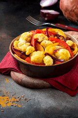 Baked spicy vegetables in a bowl on a dark background. Pepper, sweet potato, cauliflower and onion baked with cumin, turmeric, curry and ginger. Indian food, vegan food. 