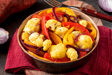 Baked spicy vegetables in a bowl on a dark background. Pepper, sweet potato, cauliflower and onion baked with cumin, turmeric, curry and ginger. Indian food, vegan food. 