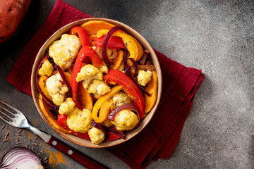Baked spicy vegetables in a bowl on a dark background top view. Pepper, sweet potato, cauliflower and onion baked with cumin, turmeric, curry and ginger. Indian food, vegan food. Copy space
