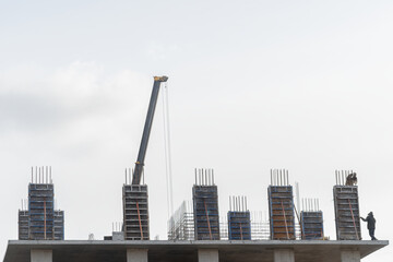 Construction of a new residential monolithic-frame house in the city using a truck crane in cloudy weather with clouds and wind