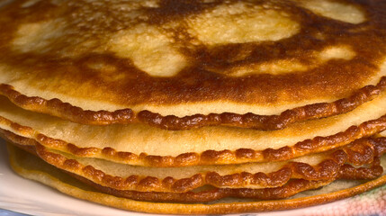 Golden pancakes lie on top of each other on a closeup plate.