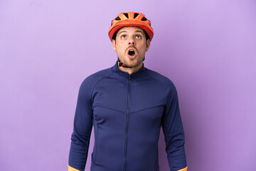 Young Brazilian cyclist man isolated on purple background looking up and with surprised expression - obrazy, fototapety, plakaty
