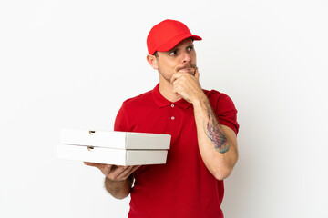 pizza delivery man with work uniform picking up pizza boxes over isolated  white wall having doubts...