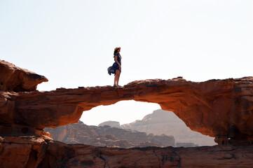 Beautiful view of the woman standing on a natural stone bridge. Wadi Rum, Jordan.