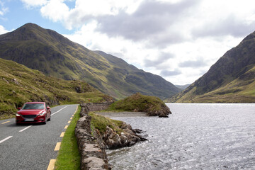 Blurred red car on the road R335, on the lakeside of Doo Lough, with Ben Gorm in the background, County Mayo, Ireland