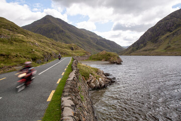 Blurred motorcycle on the road R335, on the lakeside of Doo Lough, with Ben Gorm in the background,...