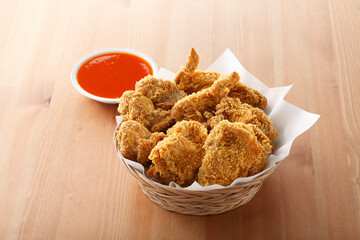 Crispy Fried Chicken in basket with chili sauce on wooden table background.