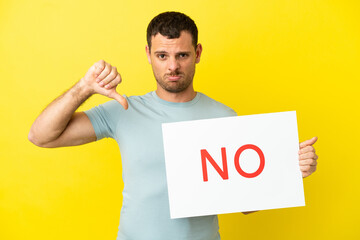 Brazilian man over isolated purple background holding a placard with text NO and doing bad signal