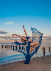 Woman blonde long hair beautiful body in a jump on the sea in the evening gymnast