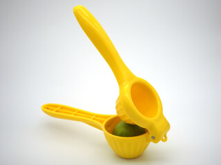 Manual citrus press. Yellow squeezer with green lemon isolated on white background