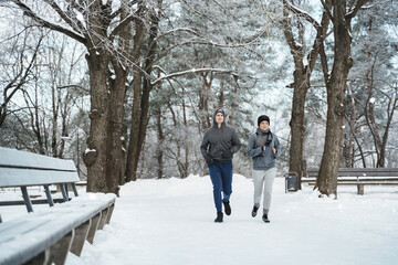 Fototapeta na wymiar Sportive couple are running in the snowy park during winter jogging workout