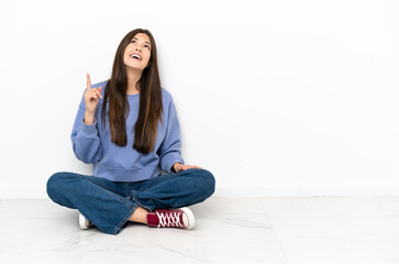 Young woman sitting on the floor pointing up and surprised