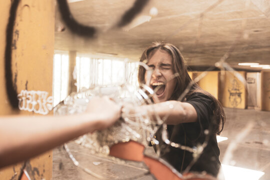 Young urban teenager girl punching and breaking a mirror in rage and relief with her bare hands and shouting out loud feeling the freedom of coming out the covid pandemic.