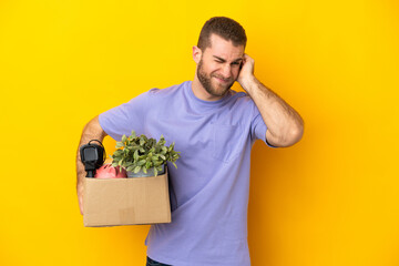 Young caucasian making a move while picking up a box full of things isolated on yellow background...