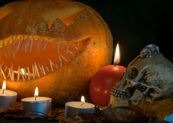 Halloween theme, carved pumpkin with a scary smile, burning candles, spiders and cobwebs, awful skulls, decoration and holiday concept, carved pumpkin for a fun party