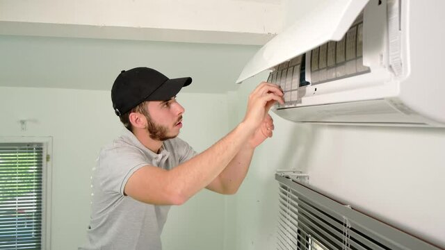 handsome young man electrician cleaning air filter on an indoor unit of air conditioning system in client house