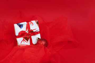 a gift for the New Year and a Christmas ball on a Christmas tree on a red background. Christmas card
