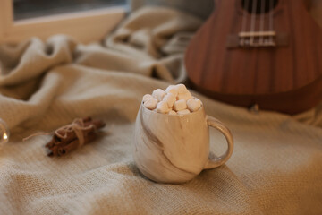 cup of cocoa with marshmallows on fabric with christmas lights and guitar