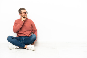 Young handsome man sitting on the floor thinking an idea while looking up