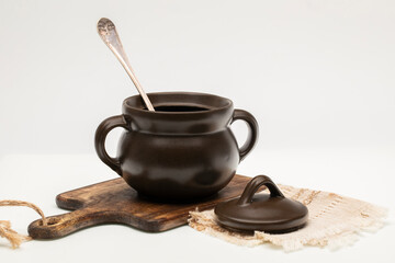 Brown ceramic cooking pot and wooden cutting board on white background