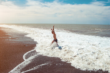 A child runs away from a wave on the seashore. Sea foam on a sunny day.