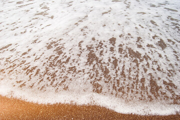 The texture of sea foam waves on the seashore. Sunny ocean shore, high tide.
