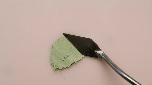 Smearing green cream on beige background, sample foundation texture close-up. Makeup and beauty products concept, cosmetics, eyeshadow palette, bronzer or concealer.