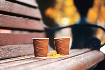 Two paper cups of coffee on wooden bench in autumn park on sunny day. Coffee time.