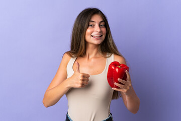 Young woman holding a pepper isolated on purple background with thumbs up because something good has happened