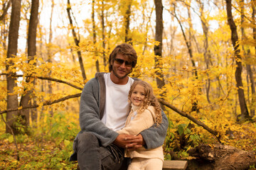 Fototapeta premium a little blonde girl in a knitted suit hugs her dad with glasses in a gray knitted jacket in the autumn forest